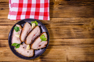 Slices of baked pork belly, garlic and parsley on a black plate. Top view