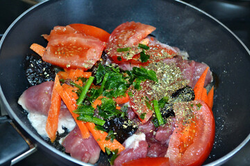 Initial braising of pork with vegetables, dried plums and spices in black braising pan. Closeup.