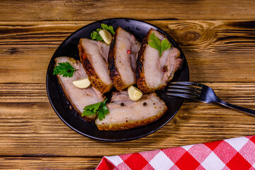 Slices of baked pork belly, garlic and parsley on a black plate