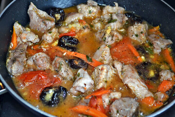 Braised pork with vegetables, dried plums and spices in black braising pan. Closeup.