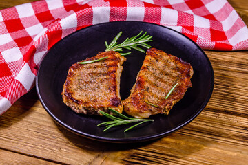 Plate with roasted steaks and rosemary twigs on a wooden table
