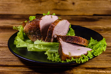 Slices of baked pork meat and lettuce leaves on a black plate