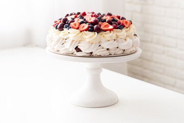 Meringue cake with whipped cream and fresh berries, strawberries, blueberries, raspberries and cherries on white table.