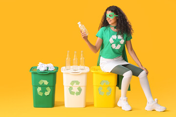Woman dressed as eco superhero with trash bins on color background