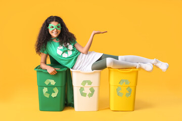 Woman dressed as eco superhero with trash bins on color background