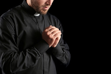 Young priest praying to God on dark background