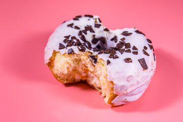 Bitten glazed donut with chocolate chip on top isolated on a pink background