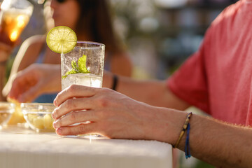 Mojito with lemon slice at a counter restaurant table. Close up on the glass and a male hand....