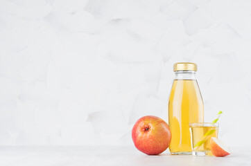 Organic yellow transperent pear juice in glass bottle mock up with straw, wine glass, fruit slice on white wood table in light interior, template for packaging, advertising, design, branding product.