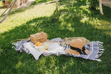 Summer picnic in a green park with cotton blanket, straw bag and hat, fresh cold lemonade and some...