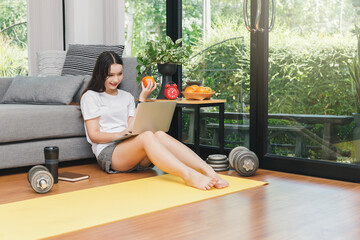 Beautiful young woman holding orange and watching fitness video tutorials online on laptop while...