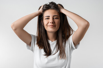 Fototapeta premium Pretty carefree modern girl with long chestnut hair holding to her head or touching hair. Isolated on white background. Emotions, expressions, hairstyle and people concept.