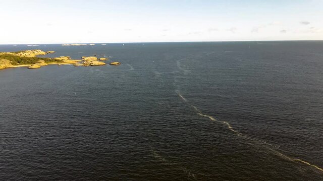 Waves creating foam on the ocean surface with sailboats and islands in the background