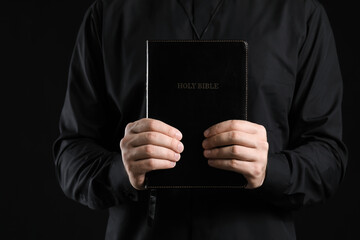 Handsome priest with Bible on dark background