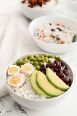 Bowl with tasty rice, beans, avocado and egg on table