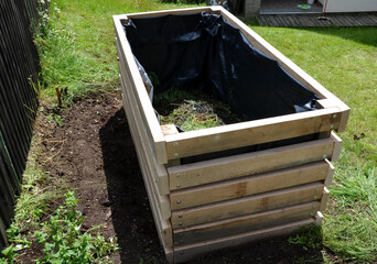 A composter made of natural beech prisms built horizontally with black foil inside in a meadow near...