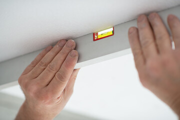 Tool level in men's hands and a flat horizontal surface of the ceiling. Styrofoam, seiling...