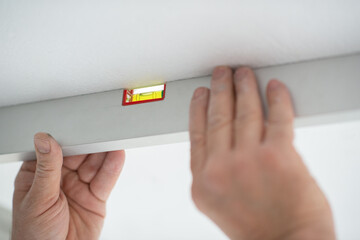 Tool level in men's hands and a flat horizontal surface of the ceiling. Styrofoam, seiling...
