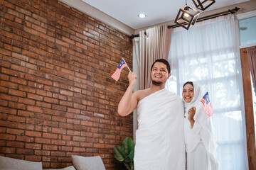 Obraz na płótnie Canvas asian wife and husband muslim holding national flag of malaysia. hajj and umrah