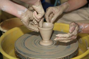 Fototapeta na wymiar Creating a clay product on a pottery wheel in a pottery workshop. Hands sliding on clay. Art