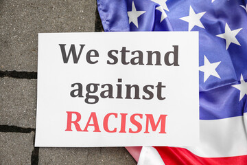 Paper with text WE STAND AGAINST RACISM and flag of USA outdoors