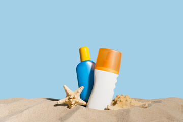 Bottles of sunscreen cream on sand against color background