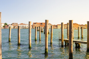 Venice, Italy. Typical landscape view of the lagoon, rawn of mooring poles in perspective with the peculiar venetian architecture in the background.