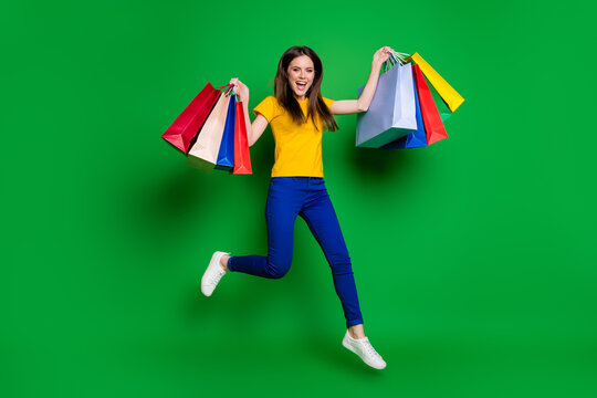 Full length body size view of nice attractive pretty glad cheerful cheery girl jumping carrying new clothes walking outlet boutique isolated bright vivid shine vibrant green color background
