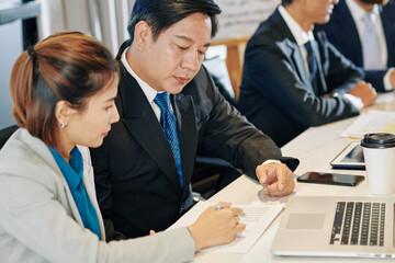 Vietnamese business colleagues discussing data in financial report at meeting