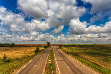 Fototapeta na wymiar Highway from the height of the bridge, against the background of clouds, fields and blue sky