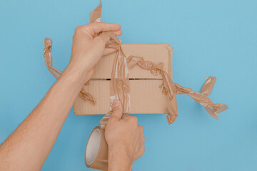 human hands try to wrap up a cardboard box with parcel tape to shut but failed