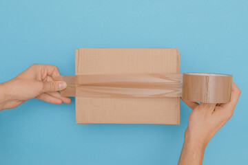 human hands wrap up a cardboard box with parcel tape