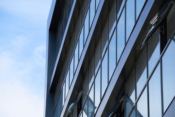 Obraz premium facade of a modern building on a bright Sunny day, blue sky and clouds reflecting in a glass, beautiful exterior of the new building