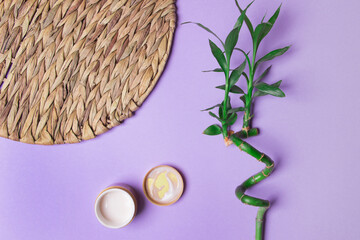opened jar with cream and bamboo and rottan circle on purple colored paper background . top view