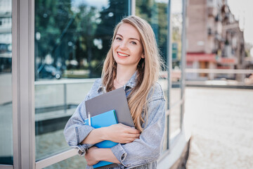 Happy caucasian girl student holds notebook folders in her hands and walks through the city...