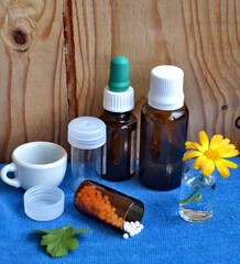 Homeopathic remedies. Alternative medicine. Homeopathic granules and pills. Marigold (Calendula officinalis in Latin) against blue background.
