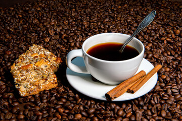 White coffee mug,  cinnamon sticks and cookies on the coffee beans background - image
