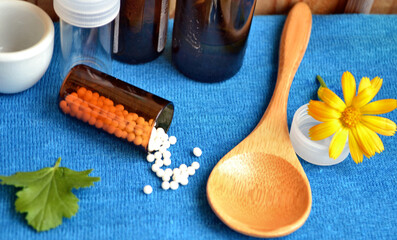 Homeopathic remedies. Alternative medicine. Homeopathic granules. Marigold (Calendula officinalis in Latin) against blue background with wooden spoon, dark and white  glass jars. 
