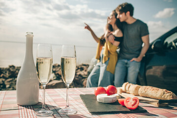 Picnic near the water. Happy family on a road trip in their car. lose-up baguette, white cheese champagne tomatoes
