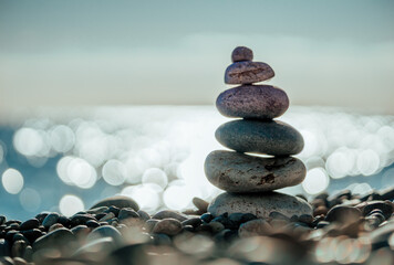 Balanced Pebbles Pyramid on the Beach on Sunny Day and Clear Sky at Sunset. Blue Sea on Background. Selective focus, Bokeh. Zen stones on sea beach, meditation, spa, harmony, calm, balance concept