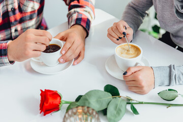Cropped photo of female and male hands stirring coffee with spoons, dating at the table in a cafe shop.