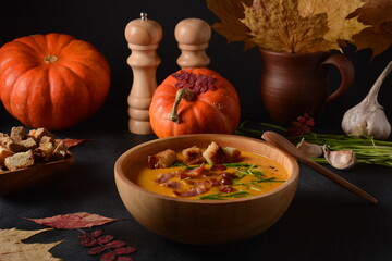Creamy pumpkin and sweet potato (batata) soup with bacon on dark background.A bowl of the soup with homemade croutons and herbs with autumn decorations.