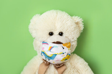 Teddy bear in a children's protective mask during the Covid-19 coronavirus pandemic on a green background