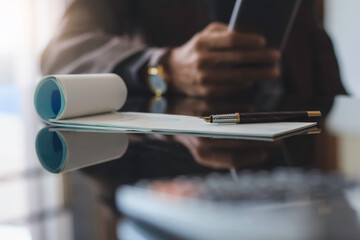 Man hand holding mobile smart phone, writing and signing checkbook with laptop computer on the desk at office. Payment by cheque concept.	