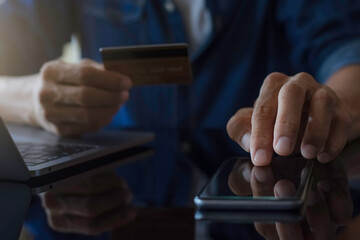 Man paying and shopping by using credit card and mobile smart phone with laptop computer and calculator on the desk at home office. e business concept.