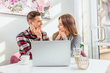 Smiling friends with a hot drink using laptop in cafe, working out a project or doing homeworl together.