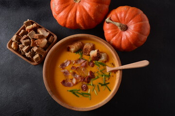 Creamy pumpkin and sweet potato (batata) soup with bacon on dark background.A bowl of the soup with homemade croutons and herbs with autumn decorations.