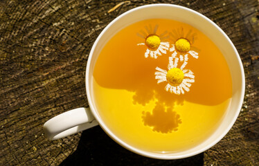 White cup with chamomile tea on a wooden stump