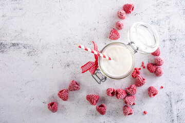 Yoghurt in glass on white wooden table decorated with iced raspberries