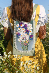 Russian fashionable girl with stylish vintage backpack. Field of wild camomiles. Flower field. Retro style in fashion. Summer day in Russia. July nature in countryside. Russian village. Natural beauty